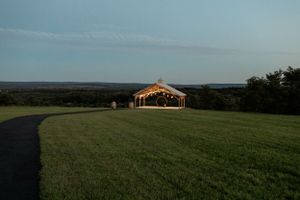 An illuminated barn venue glows at dusk on a grassy hilltop.