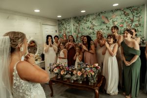 A group of bridesmaids react emotionally during a pre-wedding moment in a getting ready room.