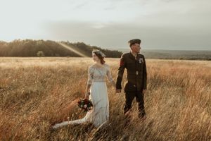 Military serviceman and bride share romantic moment in golden field at sunset.