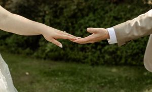 Close-up of two hands reaching toward each other during a wedding ceremony against a green background.