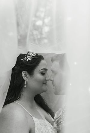 An intimate black and white portrait through a wedding veil with soft lighting and delicate details.