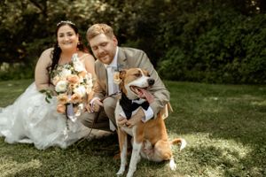 A joyful wedding portrait featuring a dressed-up dog in a bowtie on a grassy lawn.