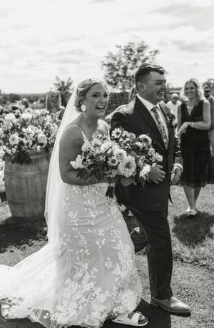 A couple walks together outdoors sharing a laugh while holding a vibrant floral bouquet.