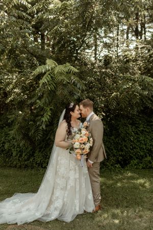 A romantic garden wedding photo with lush greenery and peach-colored floral bouquet.