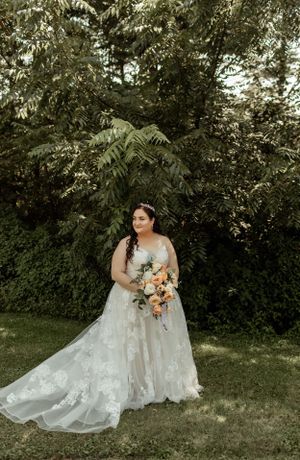A beautiful bridal portrait in a lace gown holding a peach bouquet against natural greenery.