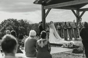 Black and white photograph of an outdoor wedding ceremony under a wooden pavilion.