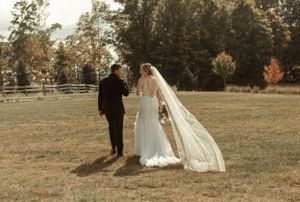 Couple walking through a rustic field during their autumn wedding with a flowing veil.