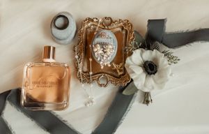 Wedding details including perfume bottle, ornate frame, and white flower on silk fabric.