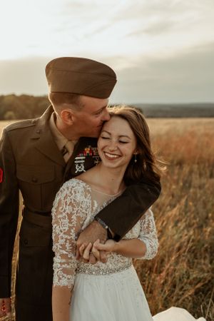 Military couple shares intimate embrace in rustic outdoor setting.