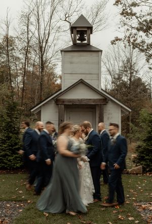 Wedding party photo in motion blur outside white chapel with bell tower.