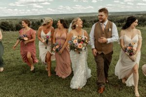 A wedding party walks through a grassy field wearing mix-matched dresses in earth tone colors.
