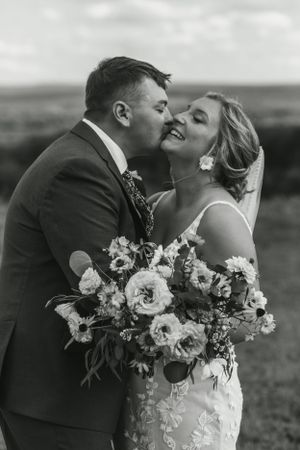 An intimate moment between newlyweds with a beautiful bouquet against a scenic landscape backdrop.