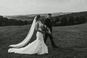 Black and white photo of a couple posing in a field with rolling hills in the background.