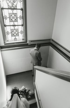 A black and white stairwell photo with stained glass window and floral bouquet.