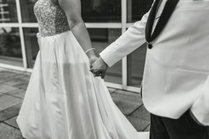 Black and white detail shot of a bride and groom holding hands showing their formal attire.