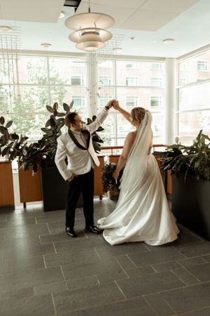A couple dancing and twirling in an elegant room with large windows and potted plants.