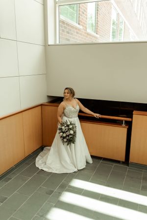 Bride in a stunning white gown holding a bouquet poses against a modern interior wall.