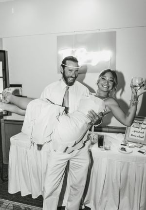 Black and white candid photo of newlyweds sharing a playful moment at their reception.