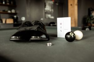 A still life of formal black shoes with billiard balls and a card on a dark surface.
