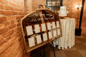 A wooden seating chart display with 'I'll Save You A Place' text against exposed brick walls.