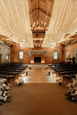 A romantic wedding ceremony space with draped fabric ceiling, string lights, and floral aisle decorations.