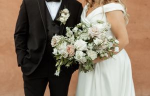 Close-up of wedding couple's attire showing black tuxedo and white dress with delicate floral bouquet.