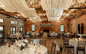 Rustic wedding reception venue with exposed brick walls, draped fabric ceiling, and elegant table settings.