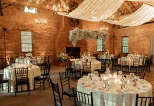 Romantic reception hall with brick walls, white draping, and round tables set for elegant dining.