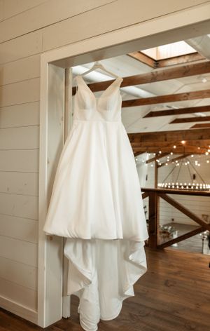 Elegant white wedding dress hanging in a rustic venue with exposed wooden beams and string lights.