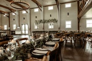 An elegant barn wedding reception setup with rustic wooden tables and hanging greenery decor.