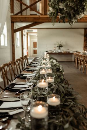 A romantic farm table setting with candles, greenery runners, and black place settings.