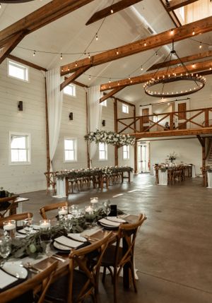 A rustic white barn venue with exposed wooden beams and string lights for a wedding reception.