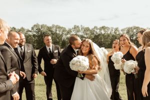 A joyous wedding party celebration outdoors with white bouquets and formal attire.