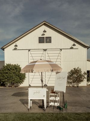 A white barn-style building exterior with an umbrella cart and signage setup outside.