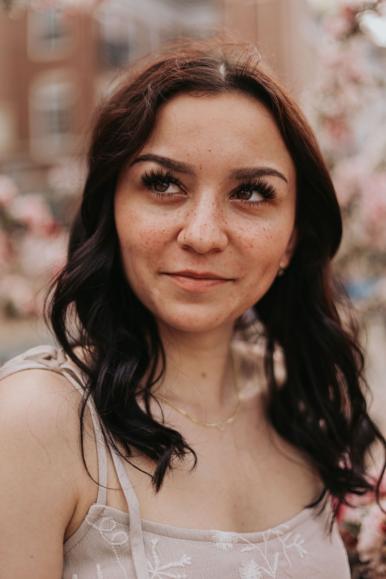 Portrait of a woman with dark hair smiling softly in natural lighting with blurred background.