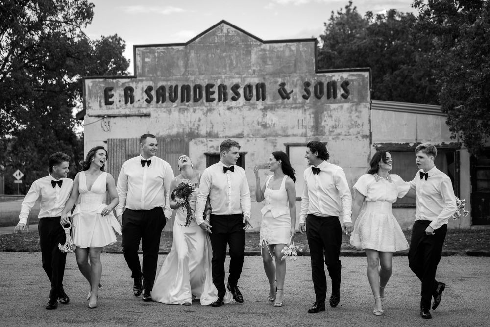 Wedding party in black and white poses in front of vintage storefront.