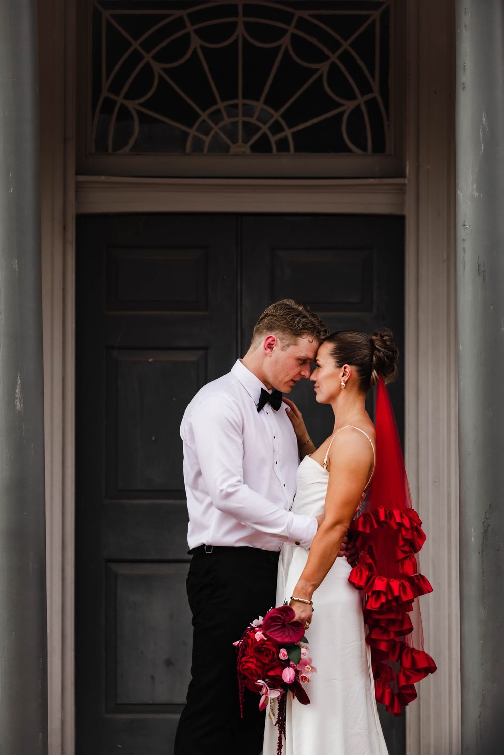 Romantic moment between couple in formal attire against dark doorway with architectural details.