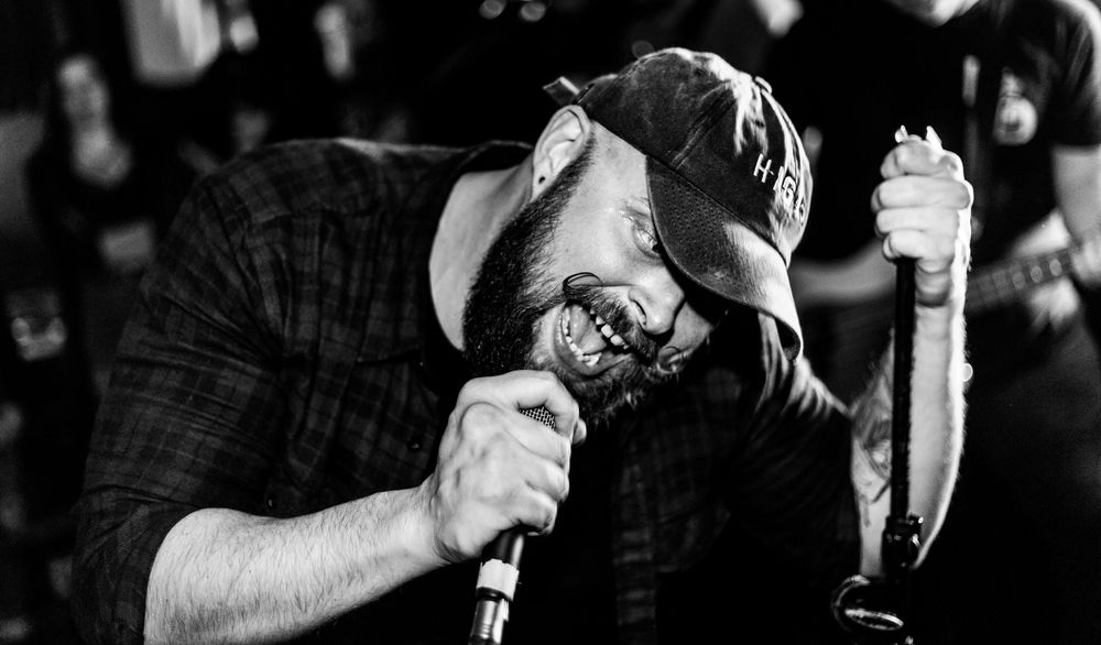 A bearded male singer passionately performs on stage in a black and white concert photo.