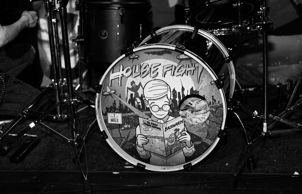 A black and white photo of a bass drum with House Fight band artwork at a concert.