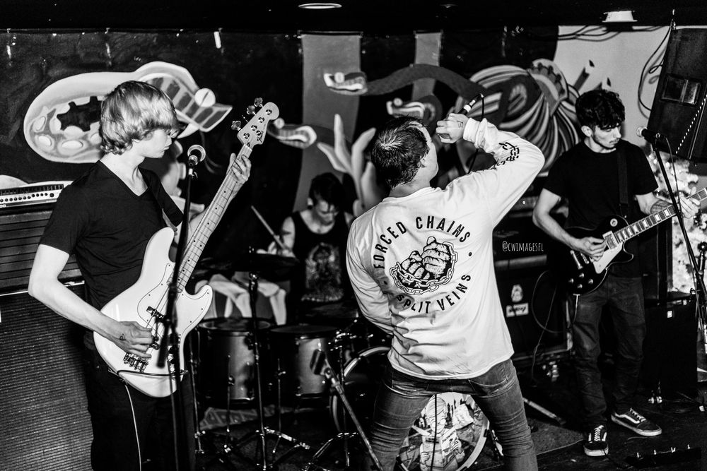 A black and white photo of an energetic punk band performing live on stage at a venue.