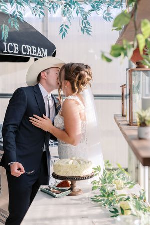 Newlywed couple sharing a romantic moment while cutting their white wedding cake at an elegant reception.