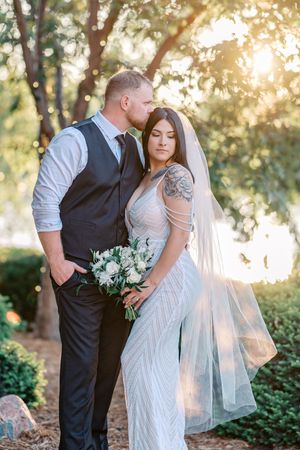 A romantic wedding couple embraces in a sunlit garden setting with lush greenery and soft golden light.