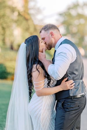 A romantic moment between newlyweds sharing kisses during their outdoor wedding celebration.