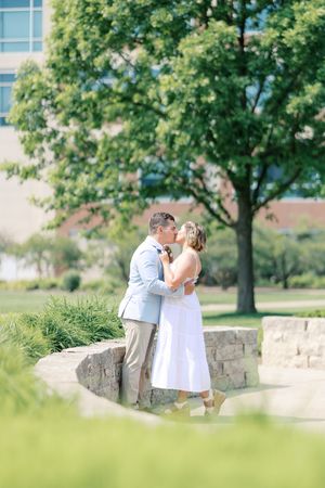 Romantic couple shares intimate moments on stone wall under green trees in summer garden setting.