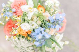 A delicate bouquet of colorful spring flowers with peach roses, blue forget-me-nots, and white daisies arranged together.