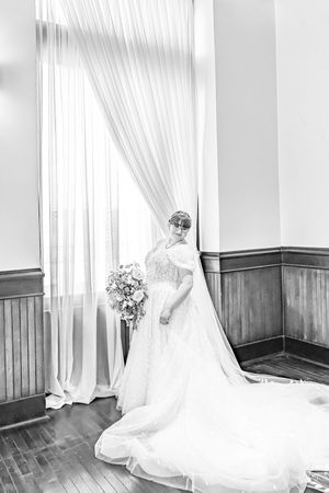 A series of elegant black and white photos showing a bride in a flowing white wedding gown against light curtains and wood panels.