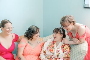 A row of bridesmaids in colorful dresses share joyful laughter while sitting together.