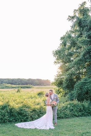 A couple embraces in a golden field at sunset with trees and nature surrounding them.