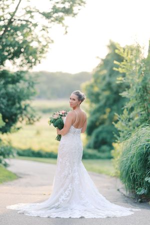 A bride in a lace wedding gown with train poses in a garden setting during golden hour.