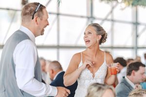 Guests mingle and dance at an elegant wedding reception in a bright, airy venue with large windows.